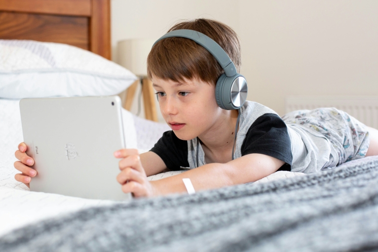 Boy on bed with headphones on and viewing iPad